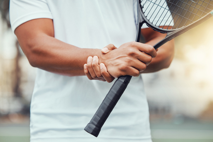 Closeup of unknown indian tennis player suffering from wrist injury in court game. Ethnic fit professional in pain while holding and rubbing hand after match. Sporty man holding racket in sports club iStock 1400627061